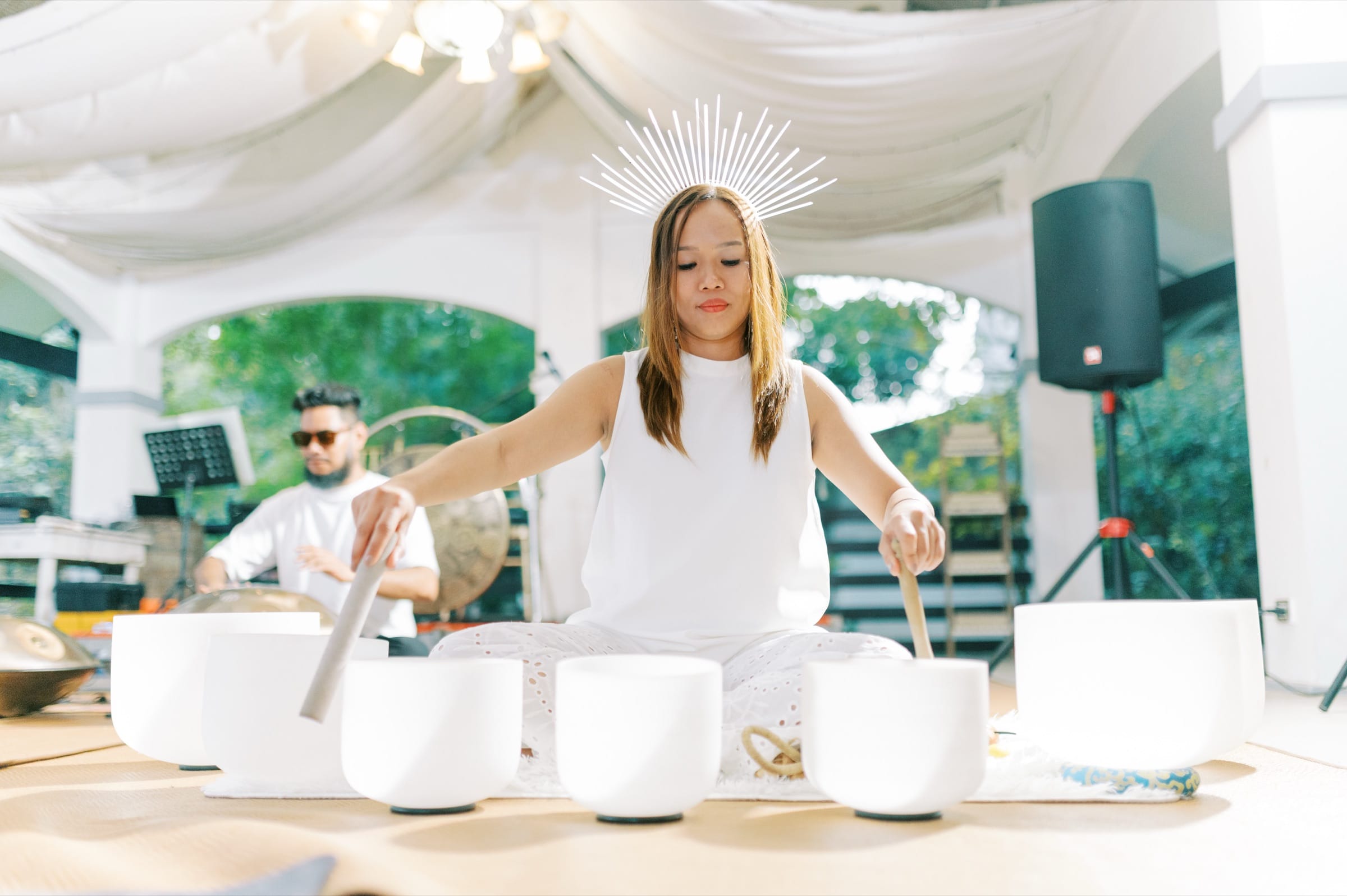 A facilitator playing crystal singing bowls, wearing a radiant sunburst crown