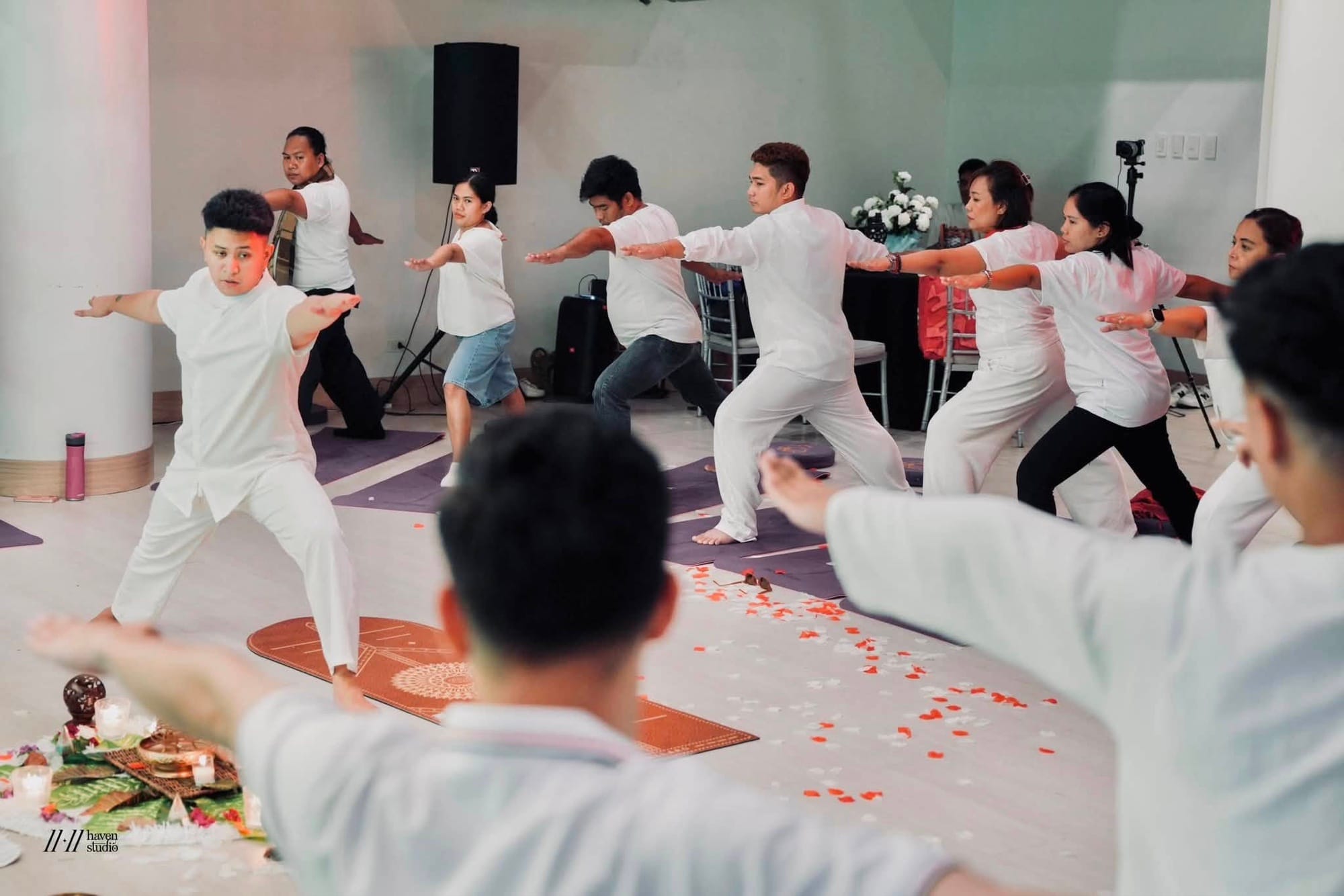 Participants moving together through a flowing warrior posture on petal-strewn floor